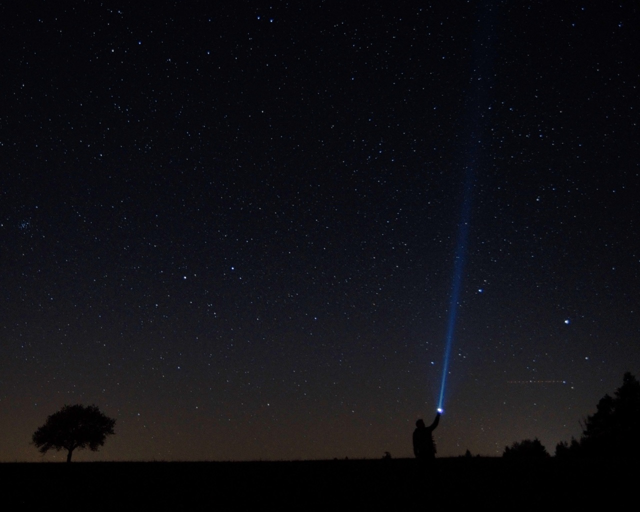 Photo: man shines a flashlight in the starry sky