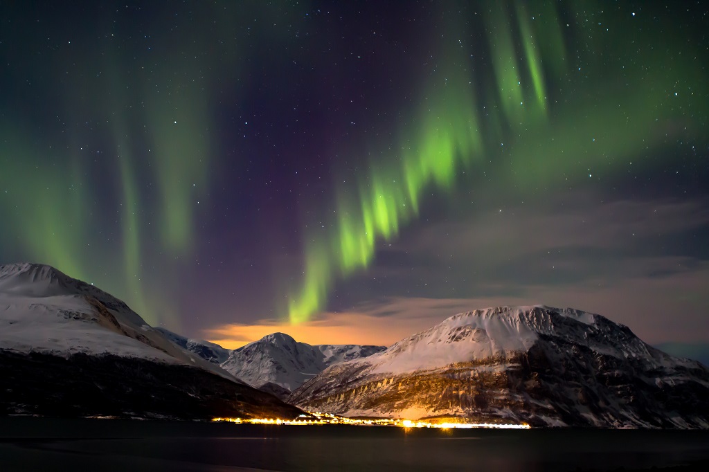 Northern lights over the mountains, under the mountain you can see the lights of the village