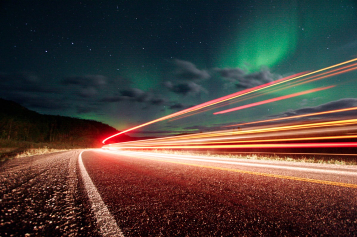 Foto de larga exposición: auroras boreales y rayas de luz en las carreteras de Alaska